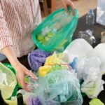 Person sorting various recyclable plastics and bottles indoors.